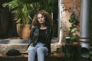 Porträt eines Teenagers, der in einem Café im Freien sitzt und mit Kopfhörern und Smartphone Musik hört - VPIF01546