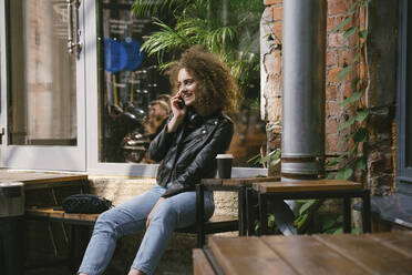 Glückliches Teenager-Mädchen am Telefon in einem Café im Freien mit Kaffee zum Mitnehmen - VPIF01550