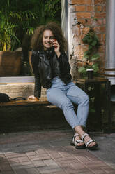 Porträt eines glücklichen Teenagers, der in einem Café im Freien sitzt und Kaffee zum Mitnehmen trinkt - VPIF01551