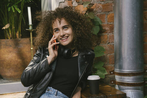 Porträt eines glücklichen Teenagers, der in einem Café im Freien sitzt und Kaffee zum Mitnehmen trinkt - VPIF01552