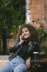 Portrait of happy teenage girl on the phone sitting at outdoor cafe with coffee to go - VPIF01554