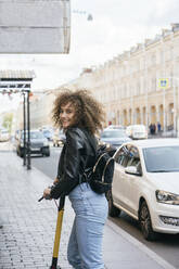Porträt eines lächelnden Teenager-Mädchens mit Roller auf dem Bürgersteig - VPIF01560