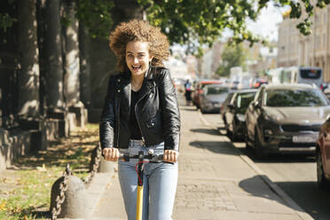 Porträt eines glücklichen Teenagers beim Rollerfahren in der Stadt - VPIF01561