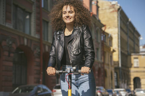 Portrait of smiling teenage girl riding scooter in the city - VPIF01565