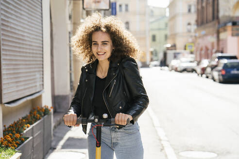 Porträt eines lächelnden Teenager-Mädchens beim Rollerfahren in der Stadt - VPIF01567