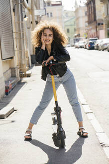 Portrait of smiling teenage girl standing with scooter on pavement - VPIF01570