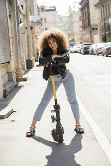Portrait of smiling teenage girl standing with scooter on pavement - VPIF01571