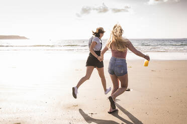 Zwei Freundinnen haben Spaß, laufen und springen am Strand - UUF19024