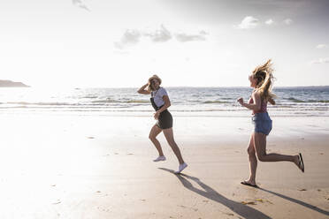 Zwei Freundinnen haben Spaß, laufen und springen am Strand - UUF19025