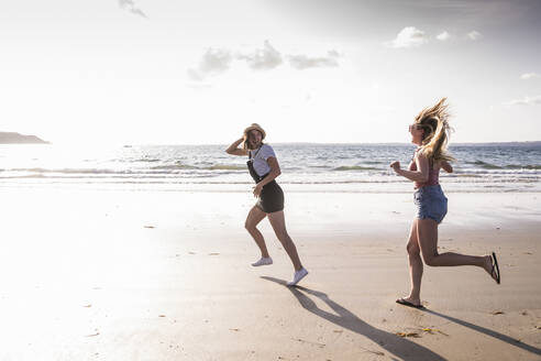 Two girlfriends having fun, running and jumping on the beach - UUF19025