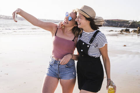 Zwei Freundinnen haben Spaß, gehen am Strand spazieren und machen Smartphone-Selfies, lizenzfreies Stockfoto