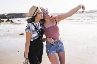 Zwei Freundinnen haben Spaß, gehen am Strand spazieren und machen Smartphone-Selfies - UUF19031