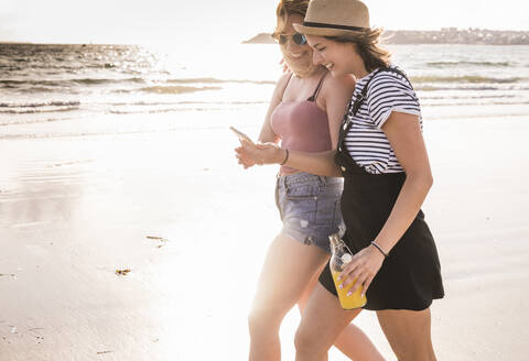 Zwei Freundinnen haben Spaß, gehen am Strand spazieren und machen Smartphone-Selfies, lizenzfreies Stockfoto