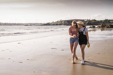 Two girlfriends having fun, walking on the beach, taking smartphone selfies - UUF19034
