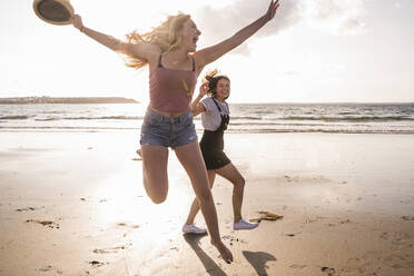 Two girlfriends having fun, running and jumping on the beach - UUF19040