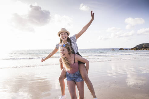 Two girlfriends having fun, carrying each other piggyback - UUF19041