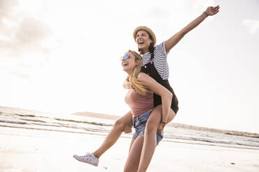 Two girlfriends having fun, carrying each other piggyback - UUF19043