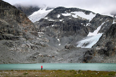 Wanderer steht am See vor Bergen und Gletscher - CAVF64833