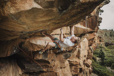 A young man climber lead climbing on an overhanging route - CAVF64850