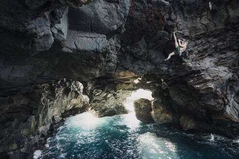 Mann klettert in einer vulkanischen Höhle über den Ozean - CAVF64851