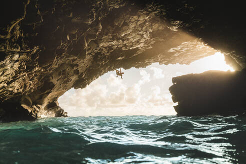 Mann klettert bei Sonnenuntergang in einer vulkanischen Höhle über den Ozean - CAVF64853