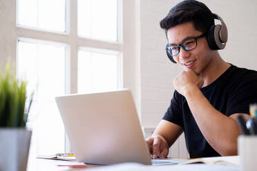 Junger Mann studiert zu Hause mit Laptop und lernt online - CAVF64910