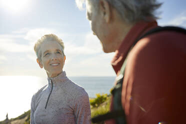 Smiling senior woman looking at man while standing against sky during sunny day - CAVF64943