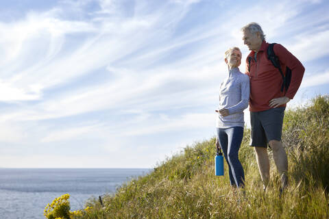 Lächelndes älteres Paar steht auf einer Klippe am Meer gegen den Himmel, lizenzfreies Stockfoto