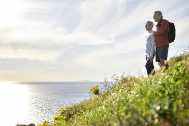 Side view of senior couple looking at sea while standing on cliff against sky - CAVF64947