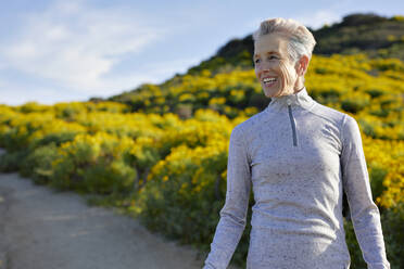 Cheerful senior woman standing on trail during sunny day - CAVF64955