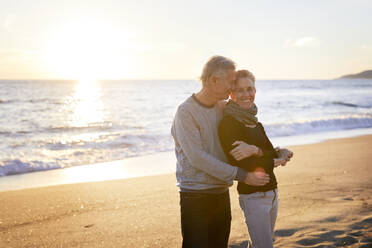 Affectionate senior couple standing at beach during sunset - CAVF64962