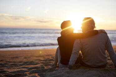 Rückansicht eines älteren Paares, das sich bei Sonnenuntergang im Sand am Strand unterhält - CAVF64966