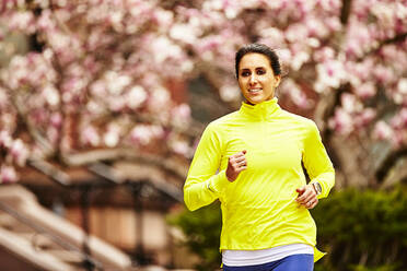 A close up of a woman running past a blossoming tree in Boston, MA. - CAVF65010
