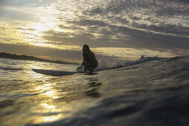 Junge Frau beim Surfen im Sonnenaufgang - CAVF65023