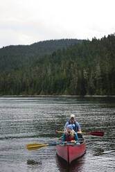 Vater und Mädchen in einem roten Kanu auf einem Bergsee in Washington - CAVF65036