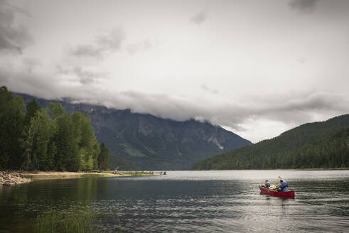 Man and Child Paddle a Red Canoe on a Mountain Lake on a Cloudy Day - CAVF65037