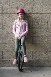 Junges Mädchen balanciert auf einem Einrad gegen eine Backsteinmauer - CAVF65045