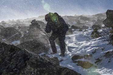 Ein Wanderer kämpft bei starkem Wind und kalten Temperaturen auf den felsigen, verschneiten Hängen in der Nähe des Mount Washington, New Hampshire. - CAVF65059