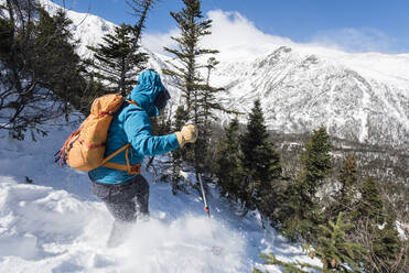 A woman hiking alone down a snowy slope with Tuckerman Ravine and the summit of Mount Washington in the background. - CAVF65062