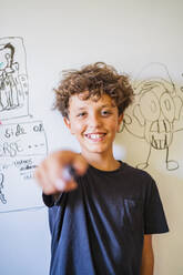 Portrait of happy boy in front of drawing on a whiteboard - DLTSF00211