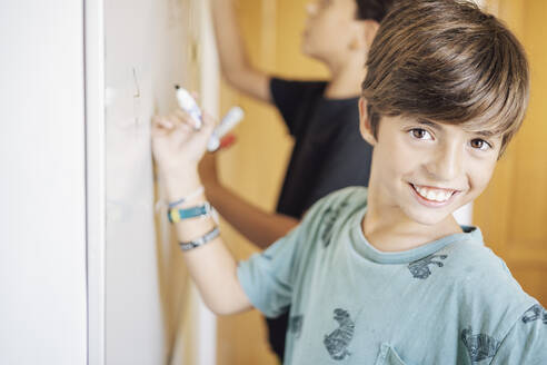 Porträt eines lächelnden Jungen mit einem Freund, der auf einem Whiteboard zeichnet - DLTSF00216