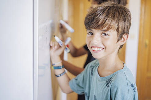 Porträt eines lächelnden Jungen mit einem Freund, der auf einem Whiteboard zeichnet - DLTSF00217