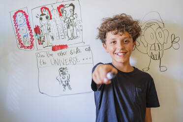 Portrait of happy boy in front of drawing on a whiteboard - DLTSF00231
