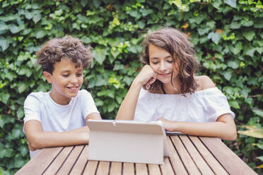 Mädchen und Junge schauen auf Tablet auf Efeu Hintergrund - DLTSF00235