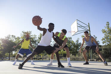 Junge Männer spielen Basketball und dribbeln den Ball auf dem Sportplatz - ABZF02607