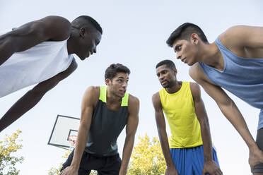 From below shot of diverse men bending forward in circle and discussing strategy of basketball game in Madrid, Spain. - ABZF02623