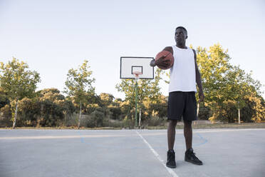 Junger afrikanischer Mann mit Basketball auf Basketballplatz - ABZF02624