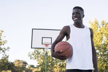 Junger afrikanischer Mann mit Basketball auf Basketballplatz - ABZF02625