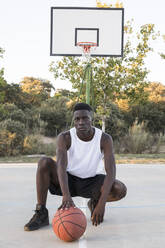 Junger afrikanischer Mann mit Basketball auf Basketballplatz - ABZF02629