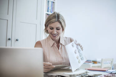 Lächelnde Frau mit Laptop, die an Modedesigns auf einem Tisch arbeitet - AJOF00024